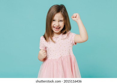 Little fun cute kid girl 5-6 years old wears pink dress doing winner gesture say yes isolated on pastel blue color background child studio portrait. Mother's Day love family people lifestyle concept