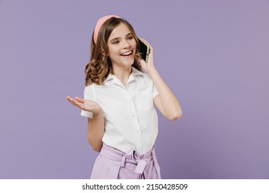 Little fun happy smiling kid girl 12-13 years old in white short sleeve shirt talk by mobile cell phone spread hand isolated on purple background children studio portrait. Childhood lifestyle concept - Shutterstock ID 2150428509