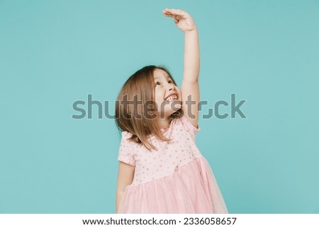 Little fun kid girl 5-6 years old wears pink dress hold hand above head show how much she grown try to be taller isolated on pastel blue color background child studio. Mother's Day love family concept