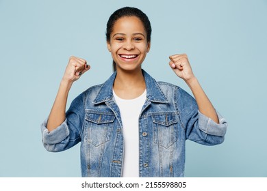 Little Fun Kid Teen Girl Of African American Ethnicity 12-13 Years Old In Denim Jacket Doing Winner Gesture Celebrate Clenching Fist Isolated On Pastel Plain Light Blue Background. Childhood Concept