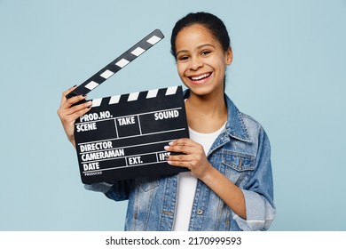 Little fun kid teen girl of African American ethnicity 12-13 years old in denim jacket holding classic black film making clapperboard isolated on pastel plain light blue background. Childhood concept - Shutterstock ID 2170999593