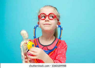Little funny blonde girl with red glasses explore the structure of human body. The skeleton of a man with insides. Early childhood development.