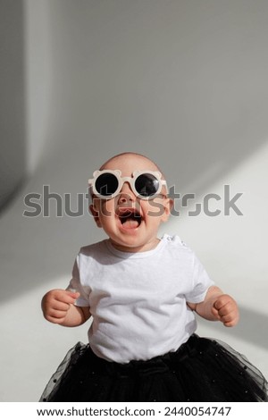 Little funny girl (1 year old) posing in sunglasses in a photo studio