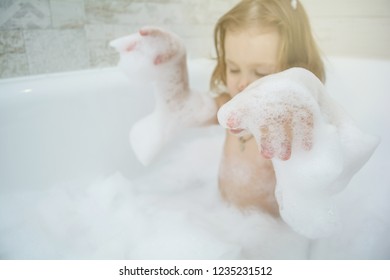 little funny girl in the bathroom playing with foam bath and smiling. Cute baby is washing her hair in bath. The symbol of purity and hygiene education