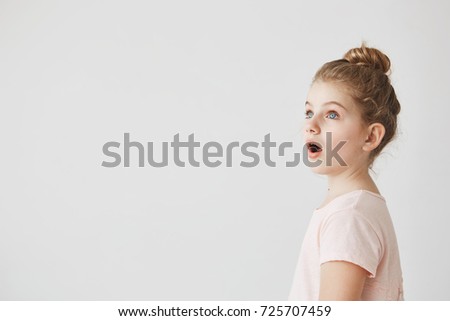 Little funny girl with blonde hair in bun standing with open mouth on street, being shocked seeing fire in neighbor's home.