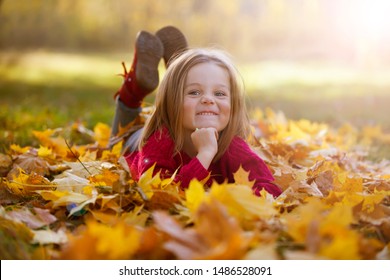 Little funny girl lies on yellow leaves in the forest. Child on a walk in the autumn park. Preschool girl on the street