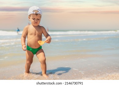 Little funny funny kid, collects shells and pebbles in the calm blue sea on a sandy bottom under the hot summer sun on a bright vacation