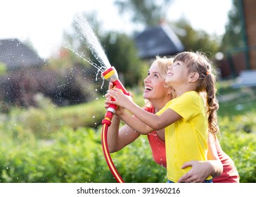 Little Gardener Girl With Mother Watering On Lawn Near House