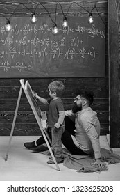 Little Genius Learning Math. Teacher Or Father Helping Kid To Solve Equation On Chalkboard. Bearded Man In Pink Shirt Sitting On The Floor.