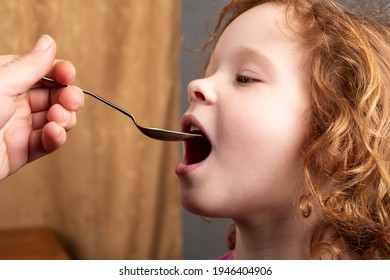 little girl 4 years old drinks cough syrup from a spoon,the child is taking medication closeup. - Shutterstock ID 1946404906