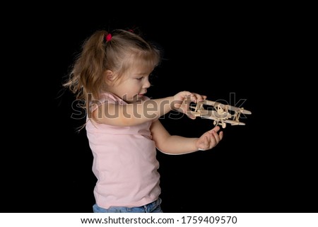 Little girl 4 years old in a light T-shirt plays with a wooden plane, dark background. travel concept