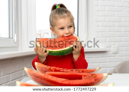 little girl 4 years old bites a big piece of red watermelon and smiles