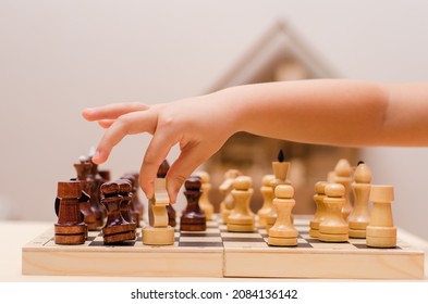 Little girl, 5 years old, enthusiastically plays wooden chess in an apartment.