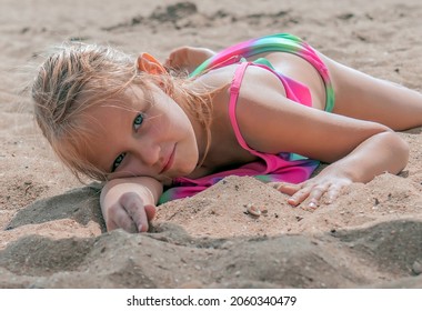 little girl 6 years old with blond hair lies on the beach in a swimsuit by the sea, portrait of a child on the seashore