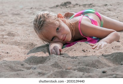 little girl 6-7 years old, blonde, lies in a bikini on the beach, on the sand, child's portrait on the seashore
