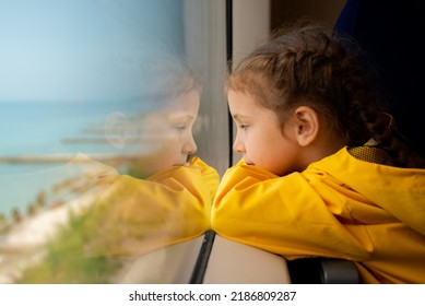 A little girl of 6-7 years old looks out the window of a train at the sea. She's wearing a yellow parka. Journey. Reflection. Vacation. Summer. Family vacation. - Powered by Shutterstock