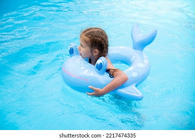 A Little Girl Of 6-7 Years Old Swims In A Pool With Blue Water. Summer. Family Vacation.