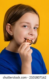 Little Girl 8-10 Years Old In Basic Blue T-shirt Biting Golden Physical Bitcoin On Yellow Background. Children Financial Literacy. Cryptocurrency And Blockchain Concept.