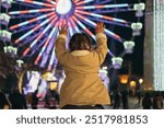 Little Girl Admiring Illuminated Ferris Wheel at Night On Her Father Shoulders. A mother and daughter gaze at a lit Ferris wheel.