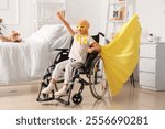 Little girl after chemotherapy dressed as superhero with yellow ribbon in wheelchair at hospital. Childhood cancer awareness concept