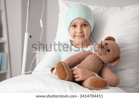 Little girl after chemotherapy with toy bear lying in clinic. International Childhood Cancer Day
