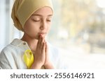 Little girl after chemotherapy with yellow ribbon praying near window, closeup. Childhood cancer awareness concept