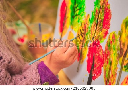 little girl artist with a brush and paints in her hands in autumn in the park draws a landscape with leaves on canvas