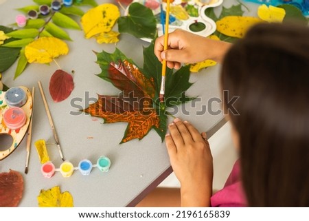 little girl artist with a brush and paints in her hands in autumn idraws a landscape with leaves on canvas