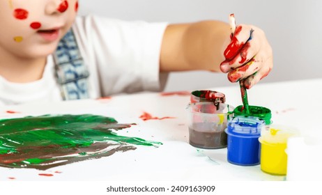 The little girl artist got her hands dirty in paint at table indoors. Children's drawings and children's development at school. The child learns to draw with paints. - Powered by Shutterstock