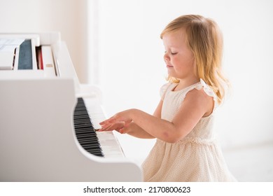 Little Girl Baby Plays A Big White Piano In A Bright Sunny Room
