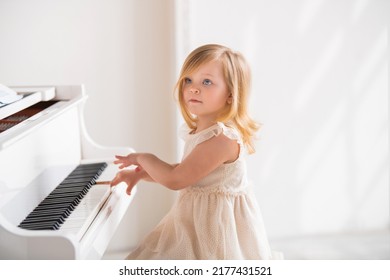 Little Girl Baby Plays A Big White Piano In A Bright Sunny Room