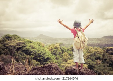 little girl with a backpack standing on a mountain top at the day time