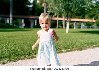 Little girl with a ball in her hand walks along the gravel path in the park