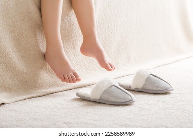 Little girl barefoot getting out of bed and wearing warm fluffy slippers on light carpet at nursery room in morning after waking up. Legs closeup. Side view. - Shutterstock ID 2258589989