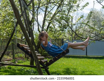 Little Girl Barefoot Rides On A Swing On A Sunny Day. High Quality Photo