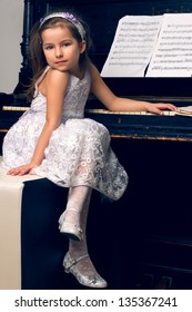 little girl in a beautiful dress sits at the piano
