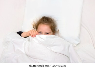 Little Girl In Bed Is Covered With A Blanket, Only Laughing Eyes Are Visible