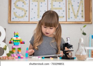 Little girl is behind the desk. Microscope, the tree, little robot and books are near her. The word STEM is on the background. E-learning. Stem education. Cute child. - Powered by Shutterstock