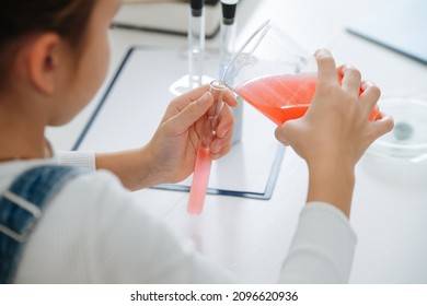 Little Girl From Behind Doing Home Science Project, Pouring Red Liquid Into A Flask From A Beaker. Over Her Shoulder.