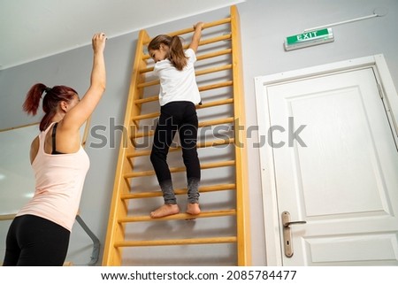 Little girl being physically active, climbing wooden ladders with instructions of her PE teacher 
