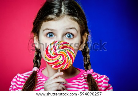 Little girl with big beautiful green eyes holding a big colorful caramel candy.