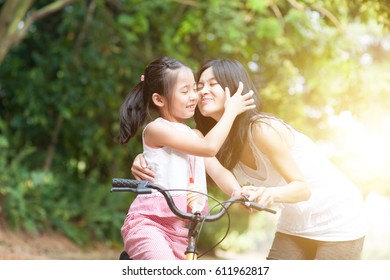 Little Girl Biking In The Park, Mother Giving A Goodbye Kiss , Asian Family Outdoor Fun Activity.