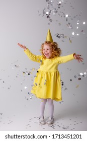 Little Girl Blonde In A Yellow Dress Catches Confeti Smiling Happy On White Background