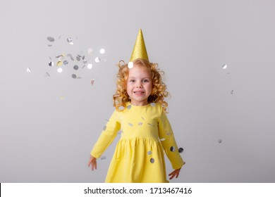 Little Girl Blonde In A Yellow Dress Catches Confeti Smiling Happy On White Background