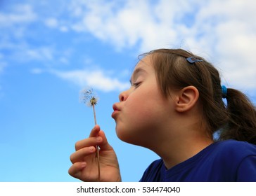 Little girl blowing dandelion on background of the blue sky