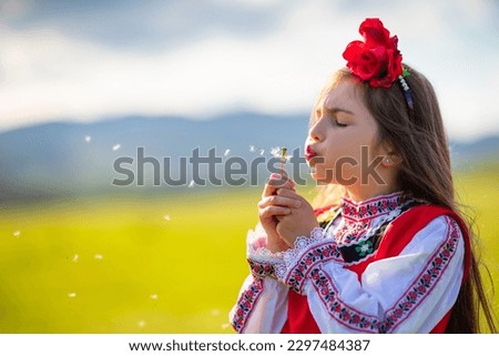 Little girl blowing dandelion on a green field. Bulgarian woman in ethnic folklore dress blow dandelions.