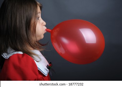 Little girl blowing a red balloon, close up portrait