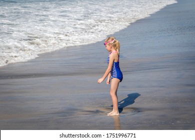 Little Girl in Blue Swim Suite Playing in Ocean Waves at the Beach