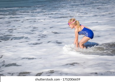 Little Girl in Blue Swim Suite Playing in Ocean Waves at the Beach