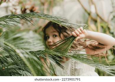 Little girl in the botanical garden. a girl in a white dress laughs near palm leaves. - Powered by Shutterstock